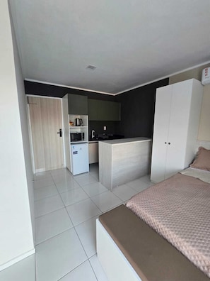 A compact bedroom with a bed, a small kitchenette, and a wardrobe. - Residencial New Stilo (Aracati)