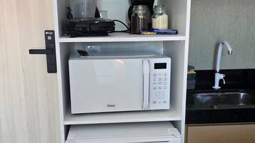 Cozinha compacta com micro-ondas embutido, pequena geladeira e máquina de café no balcão.