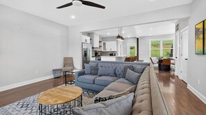 A spacious living room with a large sofa, a coffee table, and a dining area in the background. - Riverside House by Avantstay French Broad River Views Balcony Near DT + Silver Line Park (Asheville)