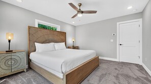 Un dormitorio con cama, ventilador de techo, mesita de noche con lámpara y una puerta.