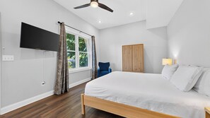 A bedroom with a bed, a television, a window with curtains, a chair, a wardrobe, and a ceiling fan. - Riverside House by Avantstay French Broad River Views Balcony Near DT + Silver Line Park (Asheville)