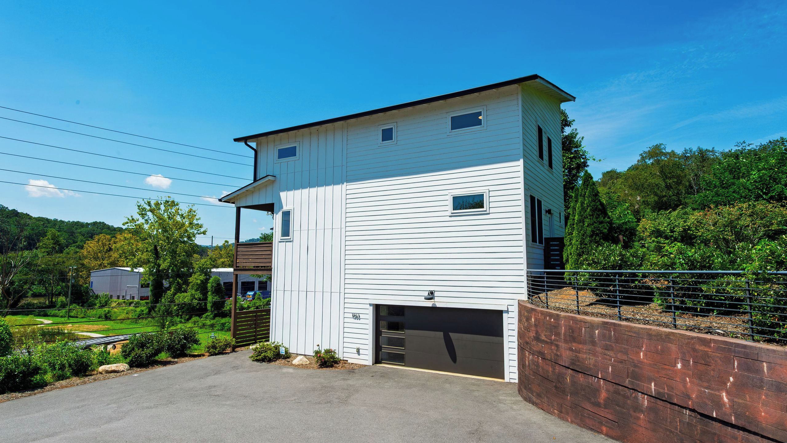 A two-story building with a garage, surrounded by greenery and a clear sky.