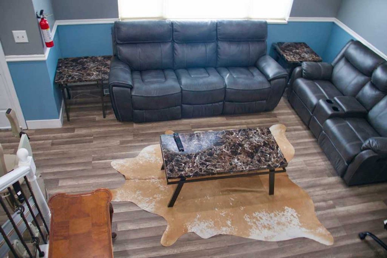 A living room with a black leather sofa, a coffee table with a marble top, and a leather pouf on a wooden floor.