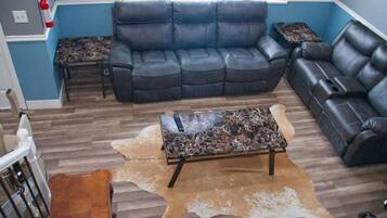 A living room with a black leather sofa, a coffee table with a marble top, and a leather pouf on a wooden floor.