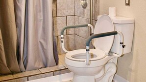 A bathroom with a shower, a toilet with a grab bar, and a window with a curtain. - Spacious, accessible family home with stair lift, full kitchen & quiet location (Provo)