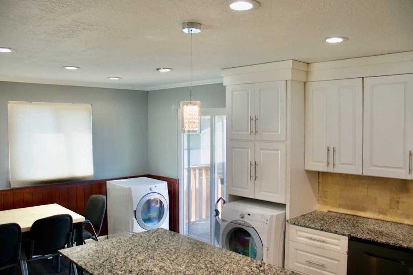 A compact kitchen with granite countertops, a built-in washer and dryer, and white cabinetry.