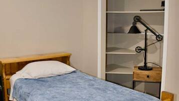 A single bed with a wooden frame and a blue blanket, a bedside table with a lamp, and a wardrobe with shelves.