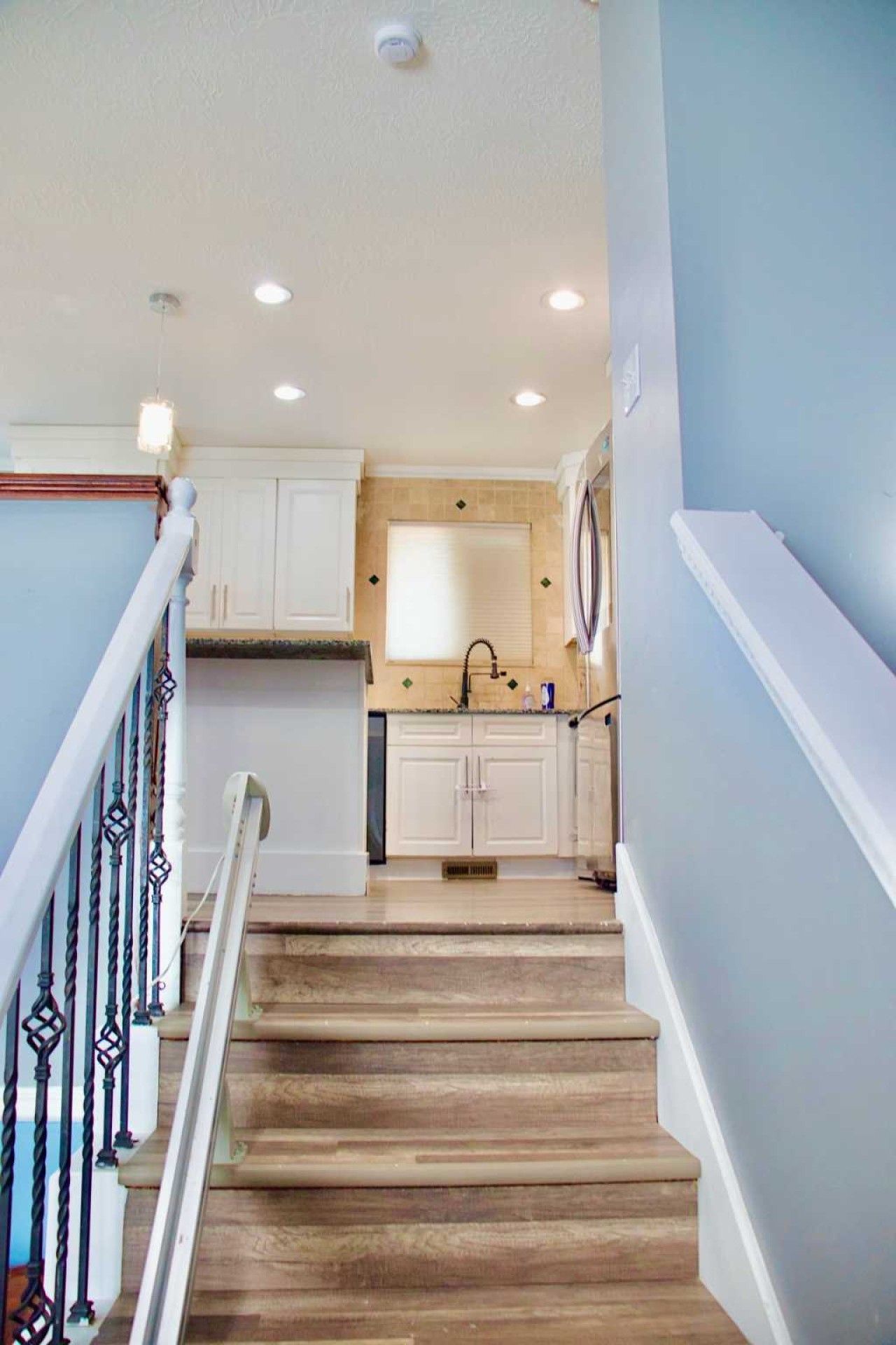 A staircase leading to a kitchen with white cabinets and a wooden floor.