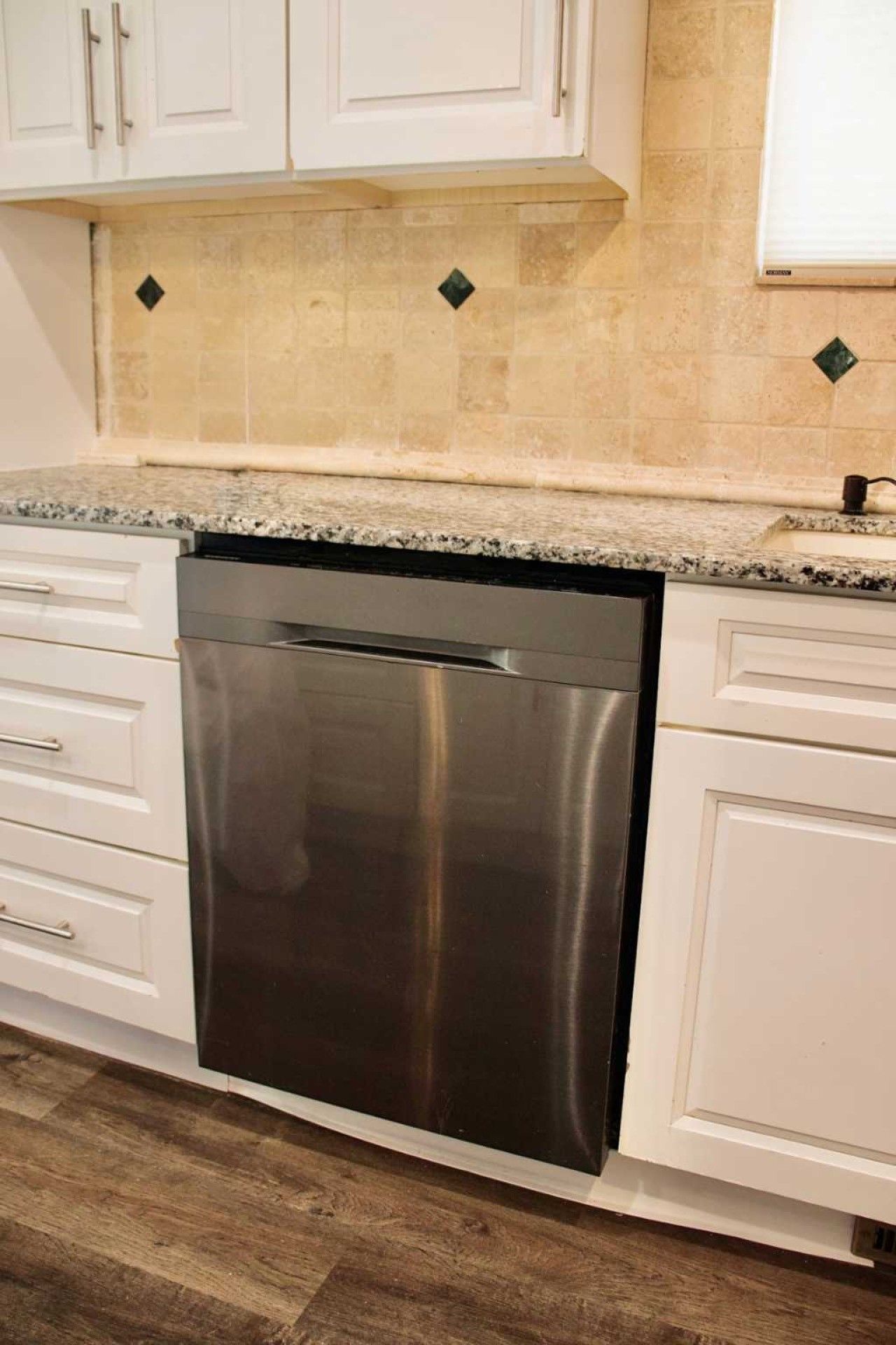 A kitchen with white cabinets, a stainless steel dishwasher, and a granite countertop.
