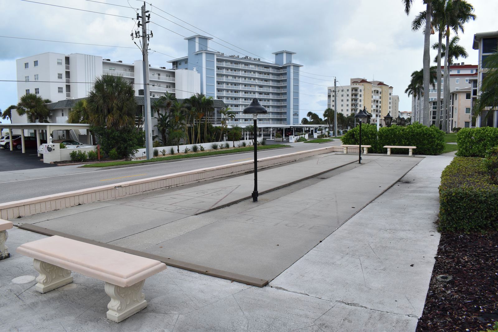 A wide pedestrian walkway with benches, a covered seating area, and a view of multi-story buildings in the background.
