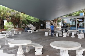 An outdoor seating area with stone tables and benches, a covered walkway, and a sign prohibiting skateboarding. - Venice Beach Getaway @ Gulf Point (Venice)