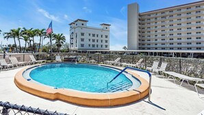 En swimmingpool med liggestole, et amerikansk flag og en hotelbygning i baggrunden.