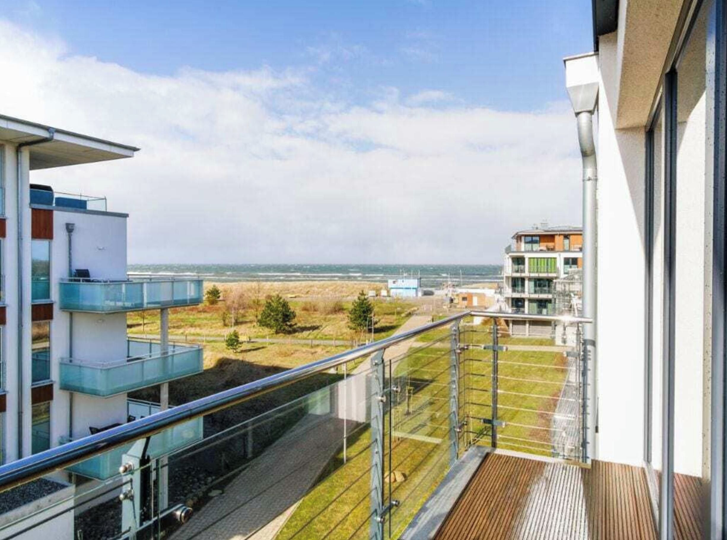 A modern building with a balcony overlooking a grassy area and a distant view of the sea.