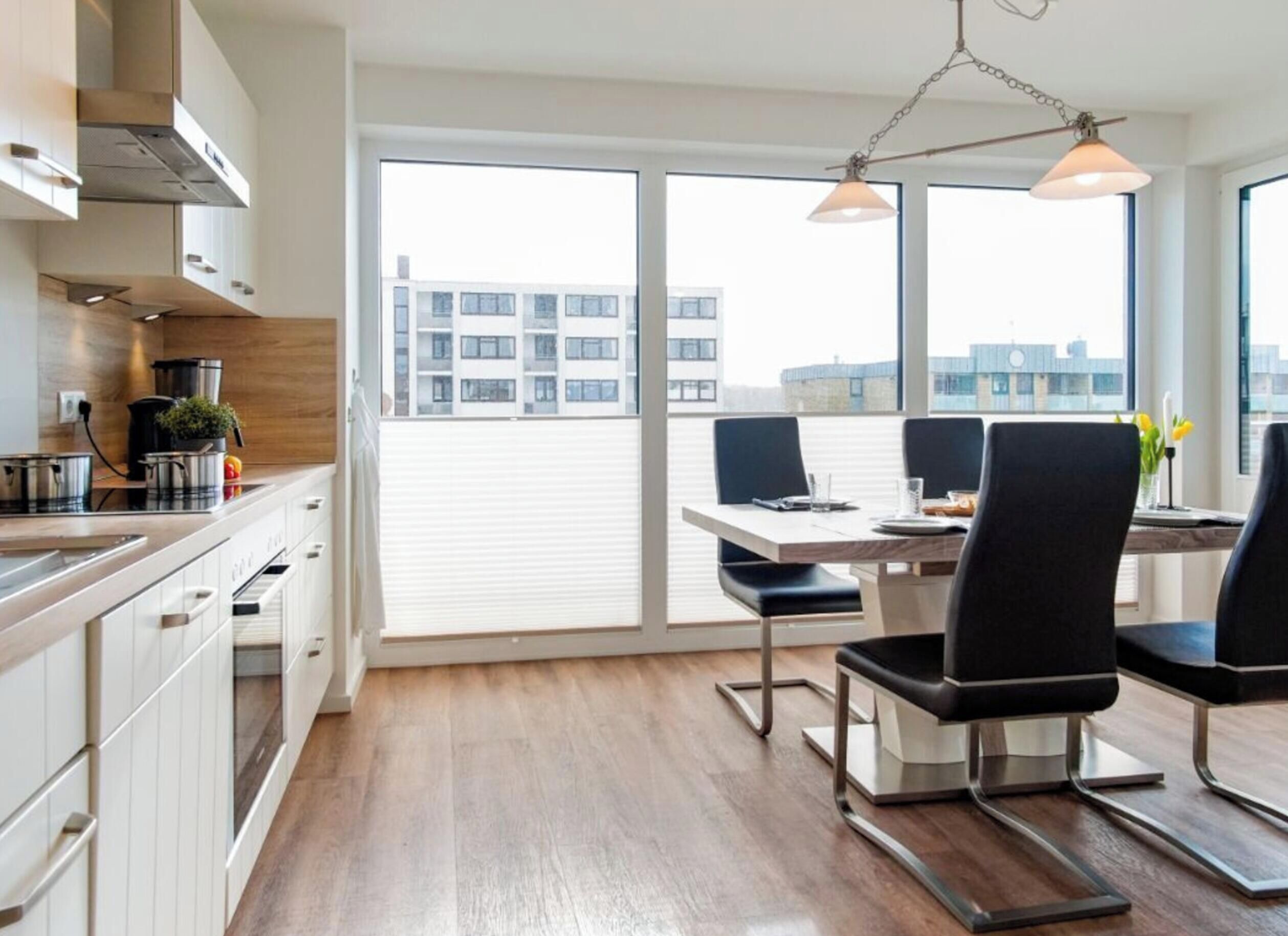 A modern kitchen with a dining area, large windows, and a view of buildings.