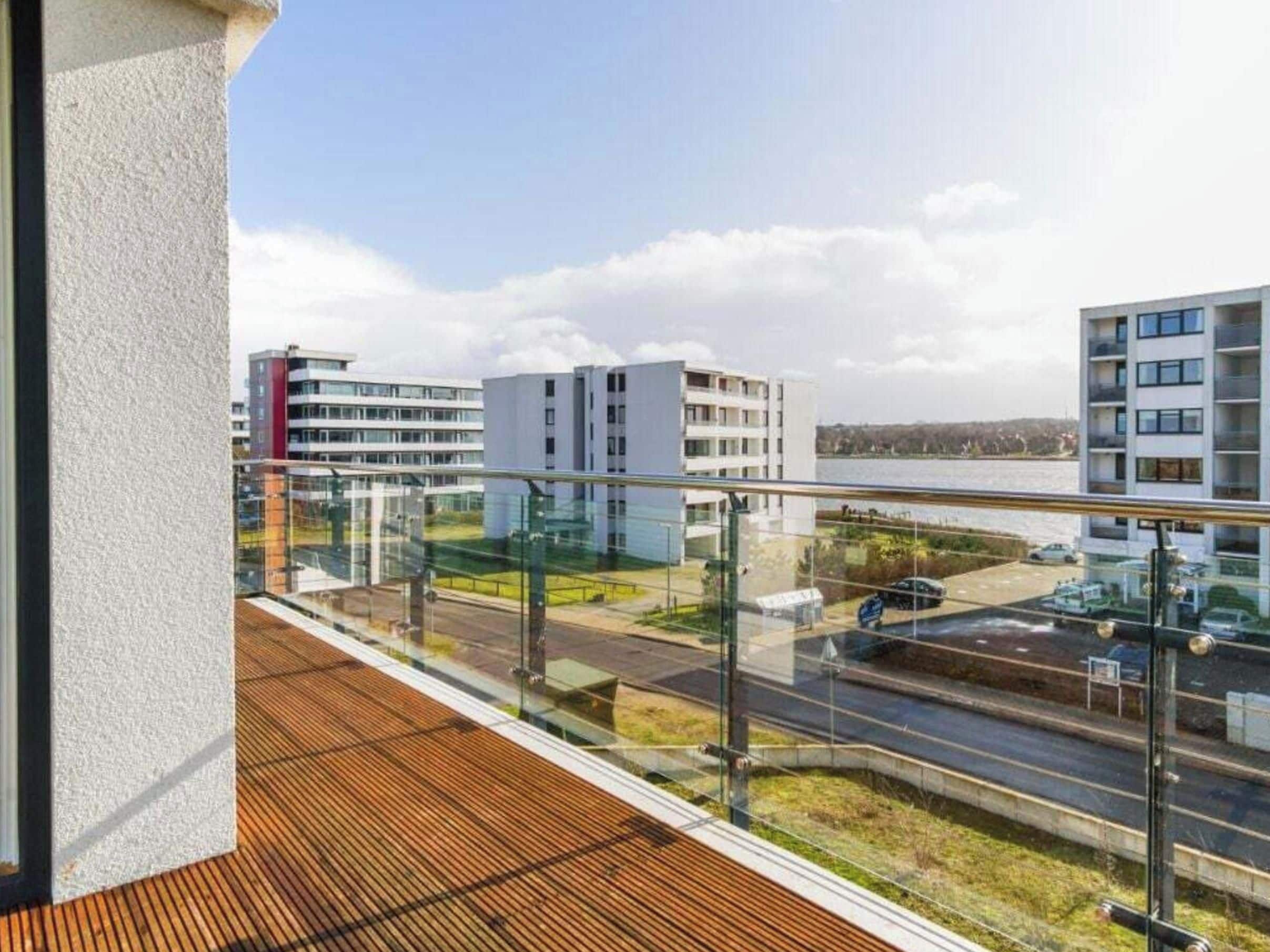 Ein Balkon mit Blick auf eine Straße und Gebäude, ein Holzboden und ein klarer Himmel.