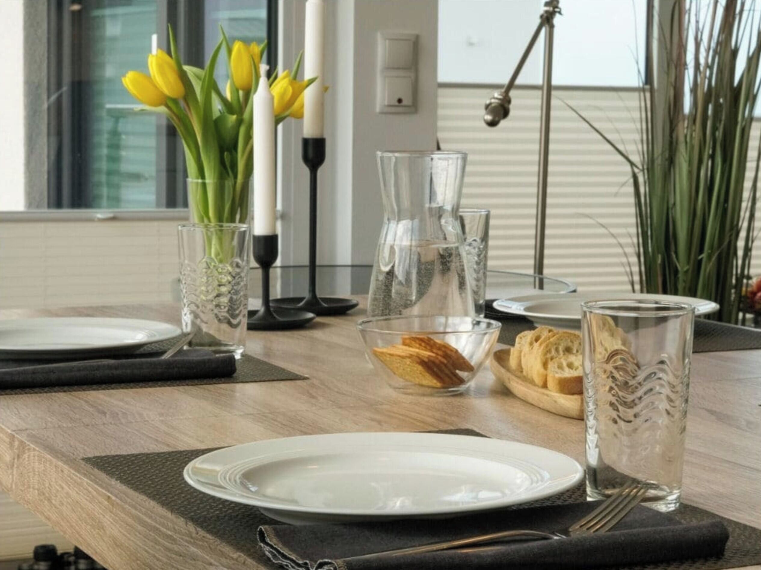 A dining table set with plates, glasses, a candle, and a vase with yellow flowers.