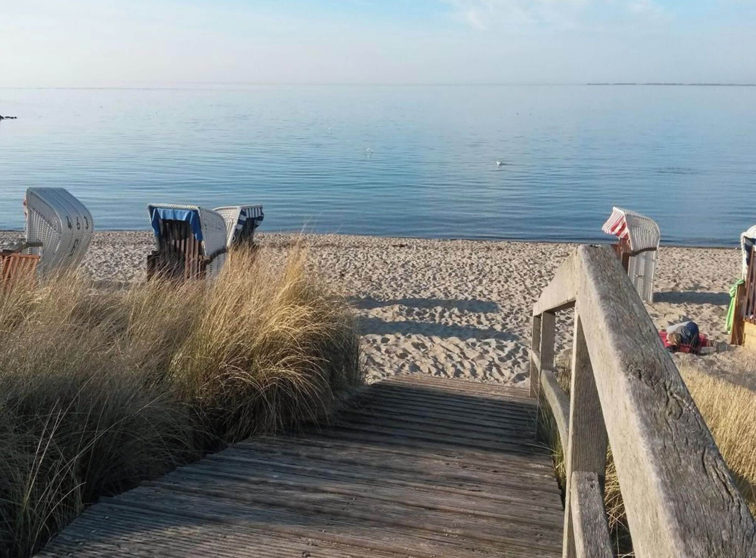 A wooden boardwalk leading to a sandy beach with beach chairs and a flag.