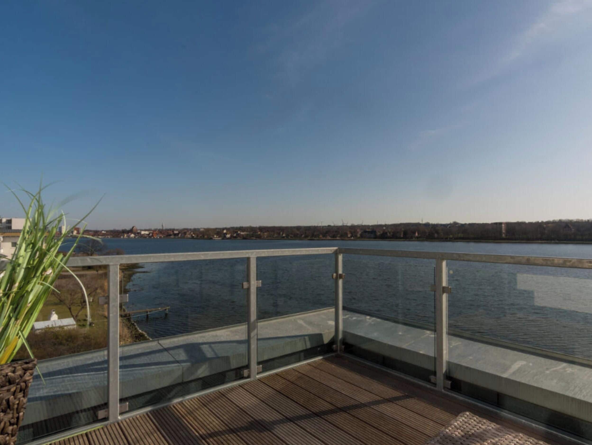 Une terrasse dotée d’une rambarde en verre, offrant une vue sur une étendue d’eau et sur une côte lointaine.