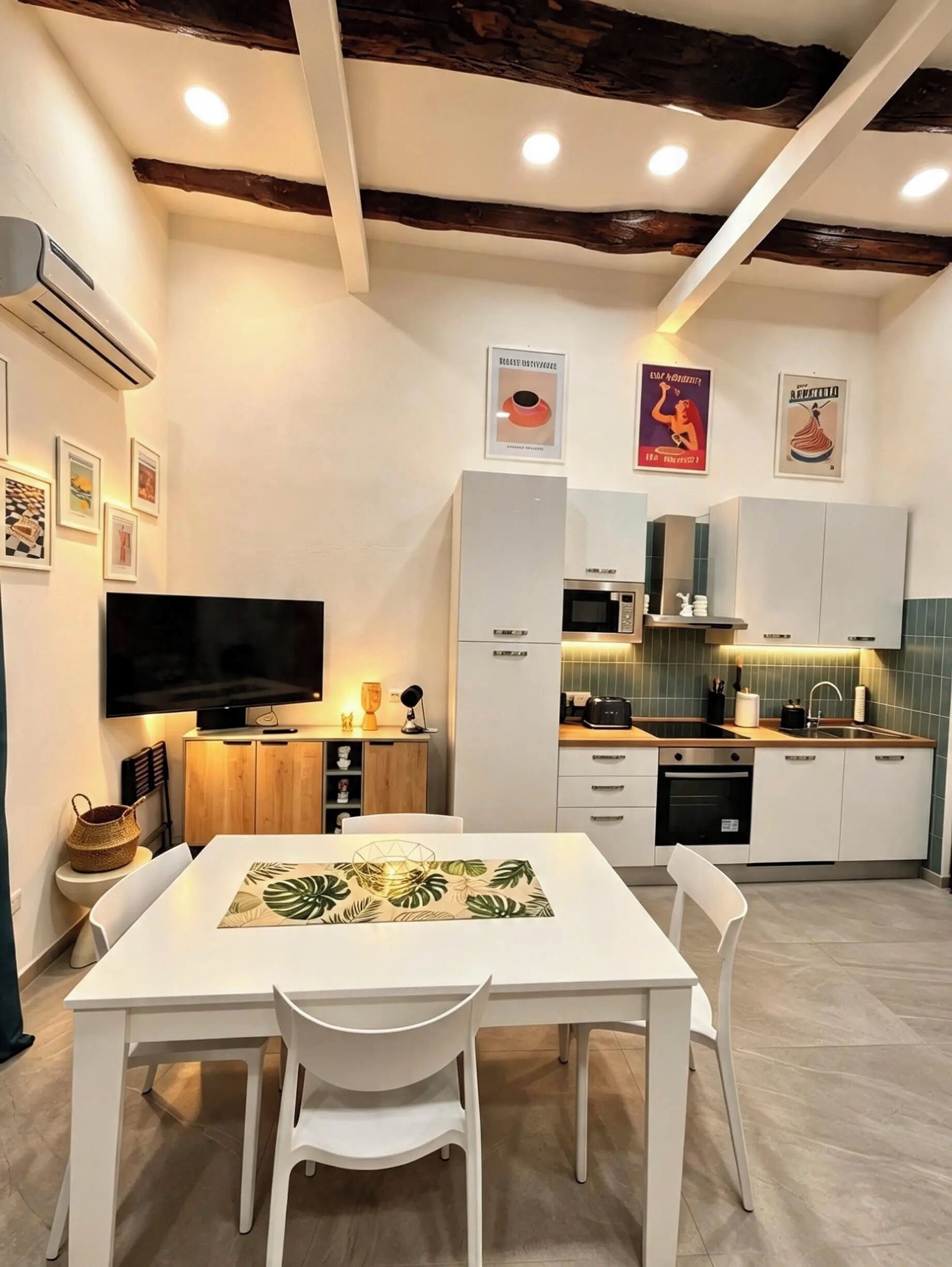 Una cocina moderna con armarios blancos, microondas y pileta. Hay una mesa de comedor con sillas y un televisor de pantalla plana montado en la pared.