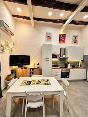 Una cocina moderna con armarios blancos, microondas y pileta. Hay una mesa de comedor con sillas y un televisor de pantalla plana montado en la pared.
