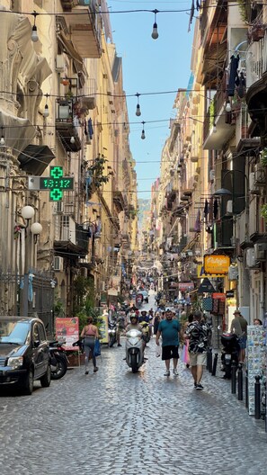Una calle adoquinada flanqueada por edificios de varios pisos, algunos con balcones y ropa tendida.