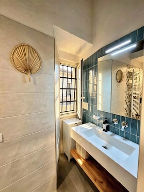 Casa de banho com um espelho grande, duas pias, uma janela e um ventilador na parede.