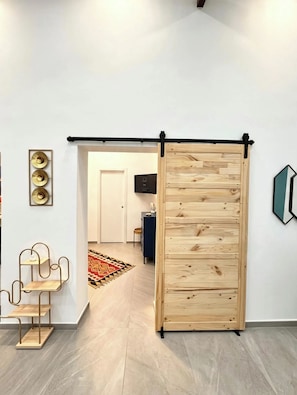 Una habitación con una puerta corredera de madera, una estantería con estructura metálica y una lámpara fijada a la pared.