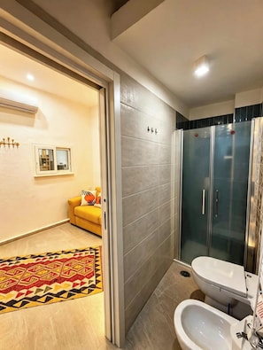 A bathroom with a shower, toilet, bidet, and a patterned rug. - RODA Apartments (Napoli)