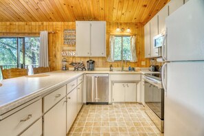 Rustic kitchen featuring wood paneling, white cabinetry, and stainless steel appliances. - Cozy Yosemite Cabin with Lake & Mountain Fun (Groveland)
