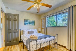 Cozy bedroom with a metal bed, ceiling fan, and tree-lined window views. - Cozy Yosemite Cabin with Lake & Mountain Fun (Groveland)