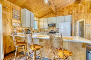 Kitchen with wooden paneling, white cabinets, and counter seating with wooden barstools. - Cozy Yosemite Cabin with Lake & Mountain Fun (Groveland)