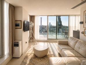 Ein modernes Wohnzimmer mit großem Fenster, einem runden Couchtisch, einer Couch und einem an der Wand befestigten Fernseher.