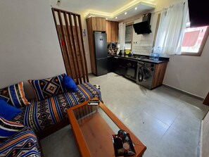 A compact living space with a sofa, a coffee table, a kitchen area with a stove, oven, and washing machine. - 🌊 New studio apartment in Martil • Self-Check-in • Secure residential complex (Martil)
