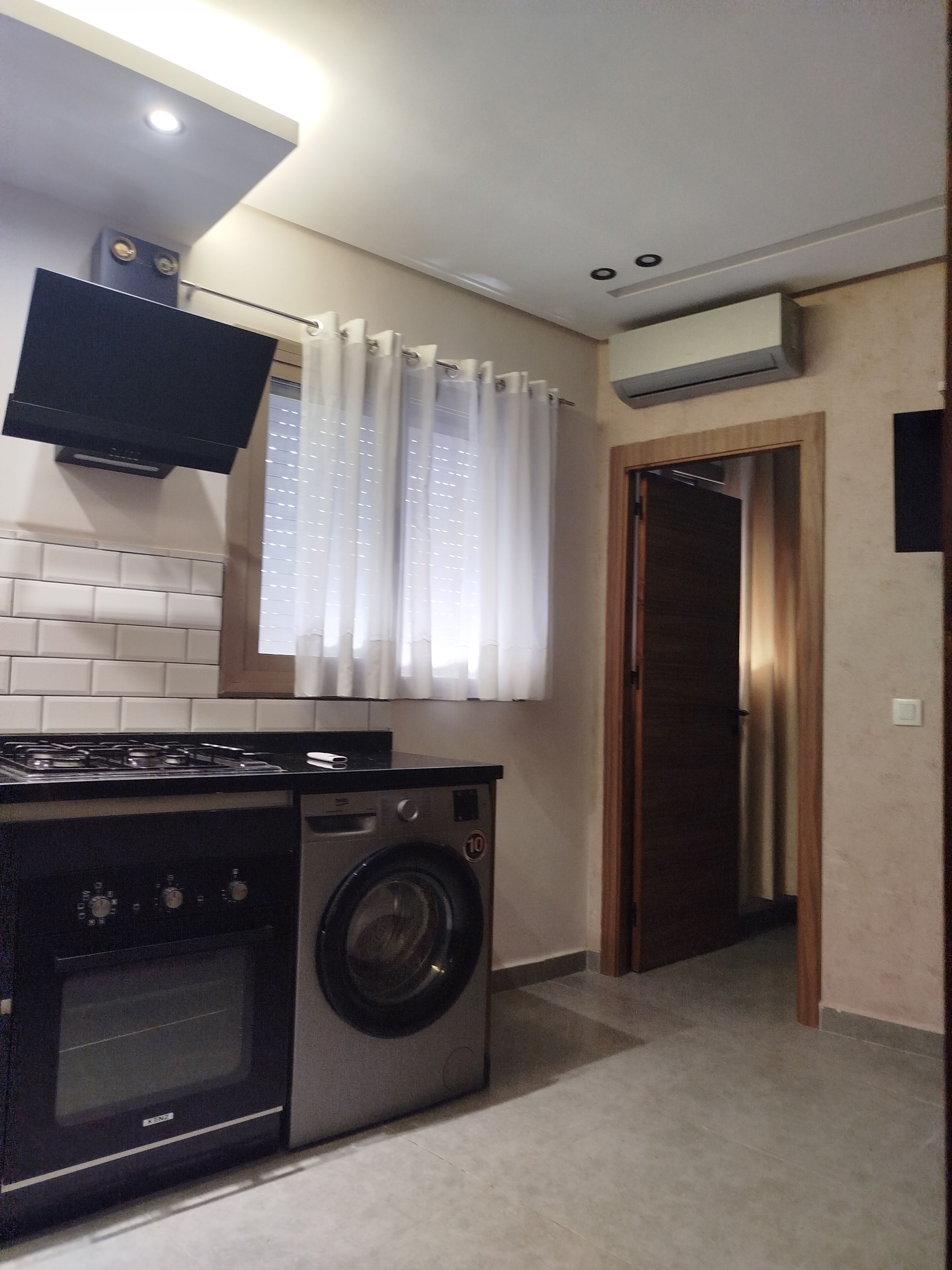 Een praktische keuken met een fornuis, een wasmachine en een flatscreen televisie boven de aanrecht.