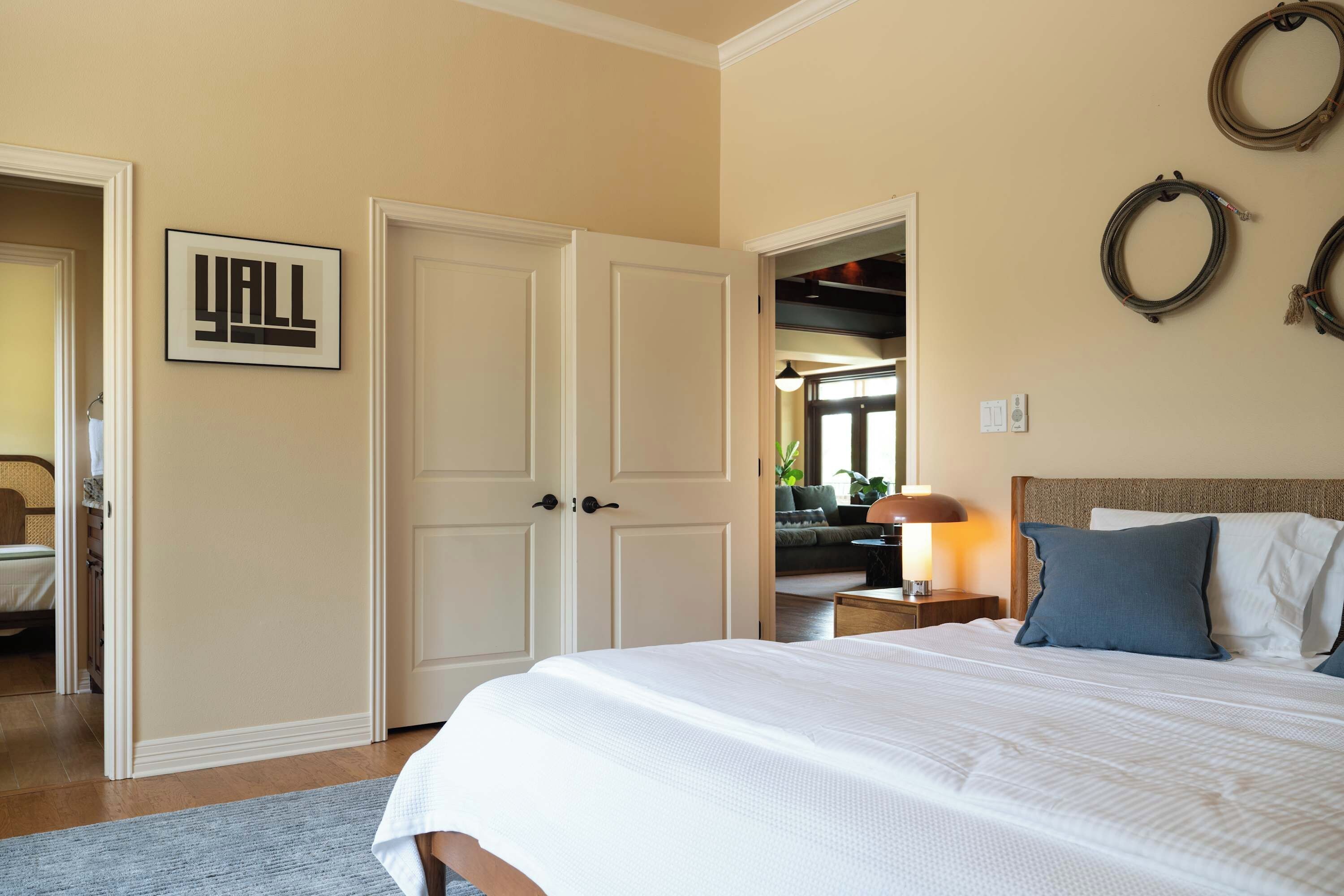 Une chambre avec un grand lit, une porte sur laquelle est affiché le mot « YALL », et une vue sur une autre pièce.