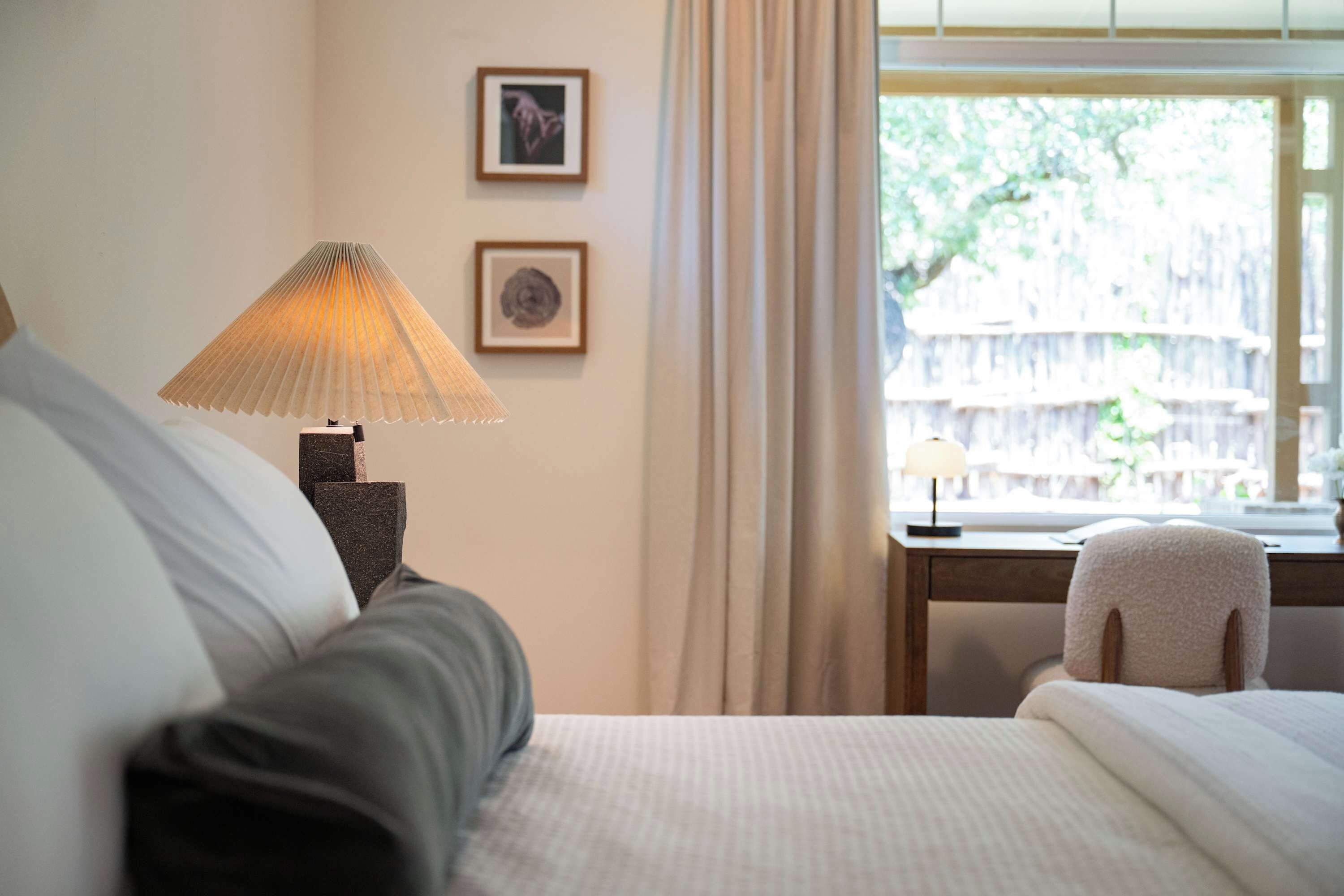 Une chambre d’hôtel avec un lit, un bureau doté d’une lampe et une vue sur la verdure environnante.