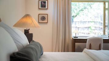 Une chambre d’hôtel avec un lit, un bureau doté d’une lampe et une vue sur la verdure environnante.