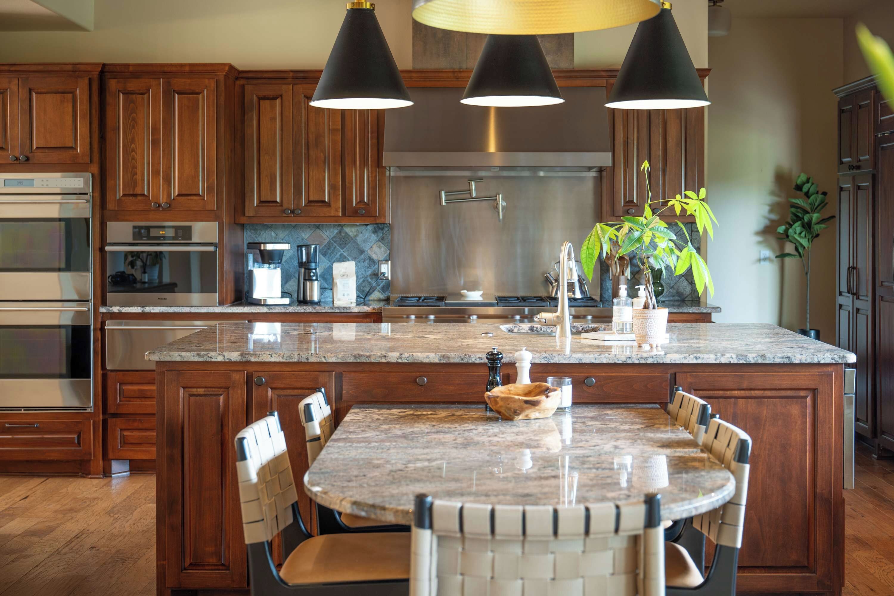 A kitchen with wooden cabinets, stainless steel appliances, a granite countertop, and a dining area with a table and chairs.