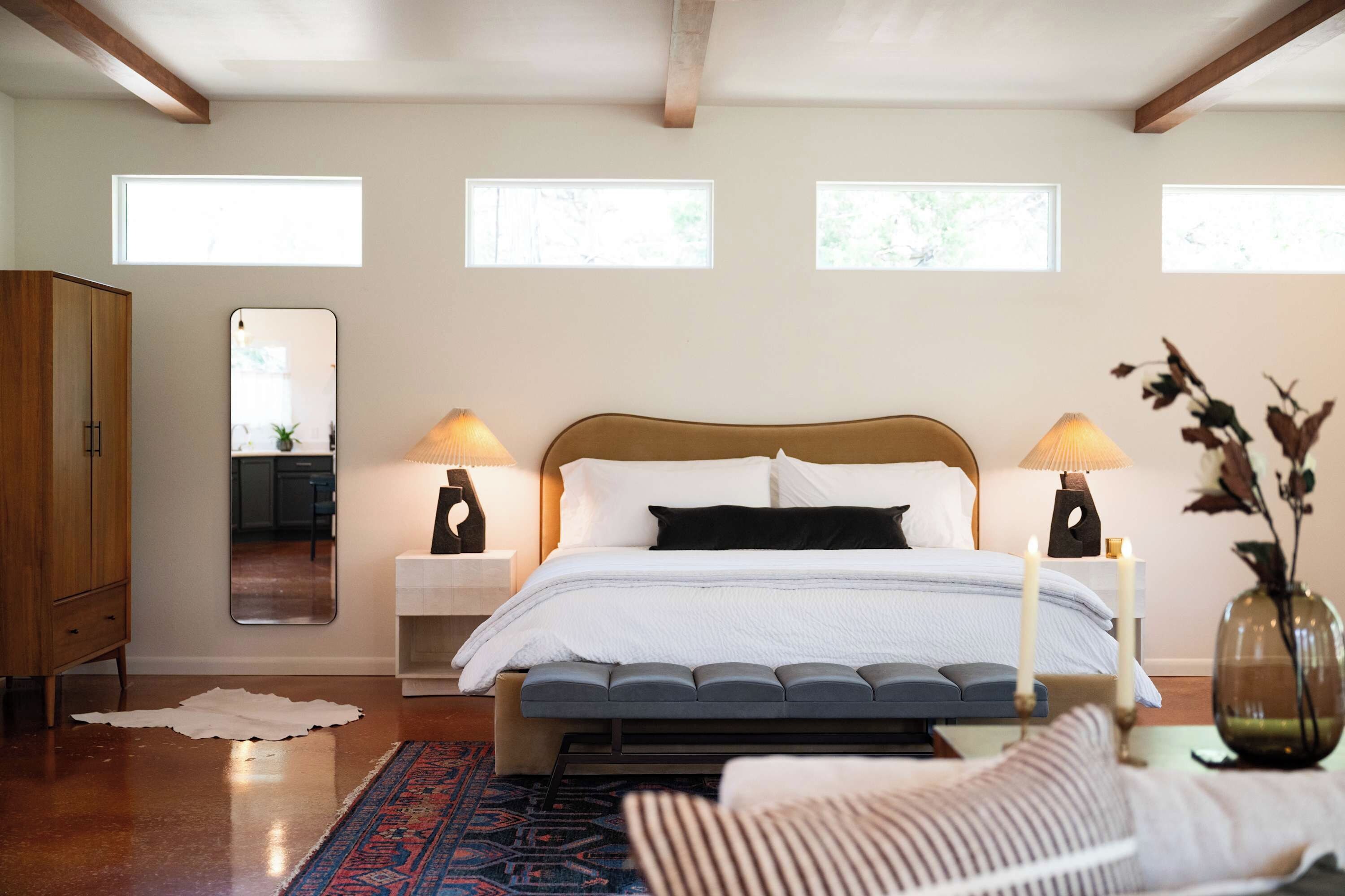 A bedroom with a bed, bedside lamps, a mirror, a wardrobe, and a rug.