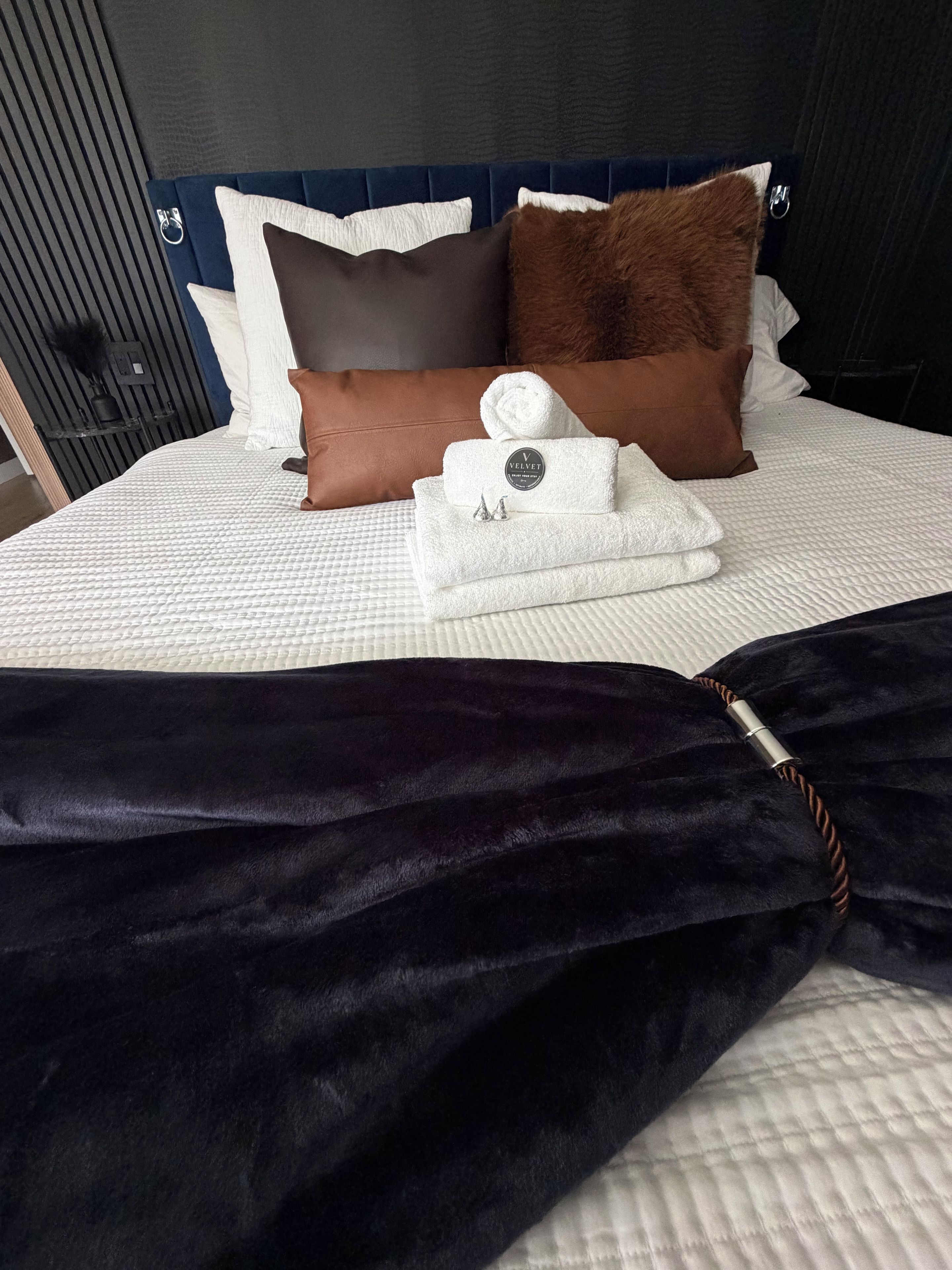 A neatly made bed with a white quilt, a dark blue headboard, and a brown pillow.