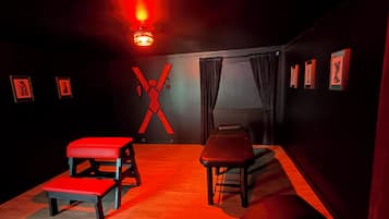 Una habitación con ambiente rojizo, que incluye un banco, una mesa y una decoración de pared con forma de X.