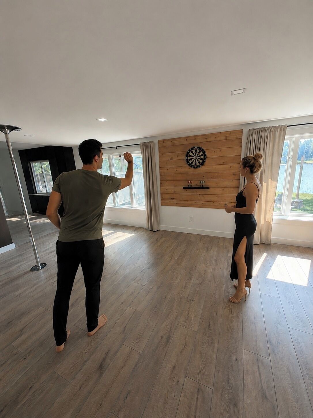 A room with a dartboard on the wall, a large window with curtains, and a modern floor.