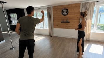 A room with a dartboard on the wall, a large window with curtains, and a modern floor.