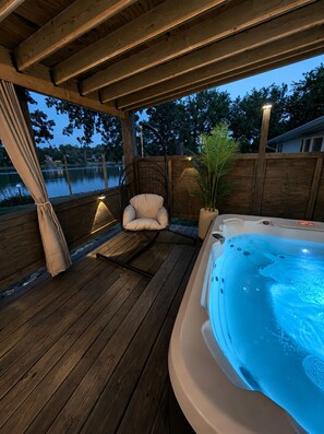 Una terraza de madera con un jacuzzi, una silla acolchada y una planta en maceta.