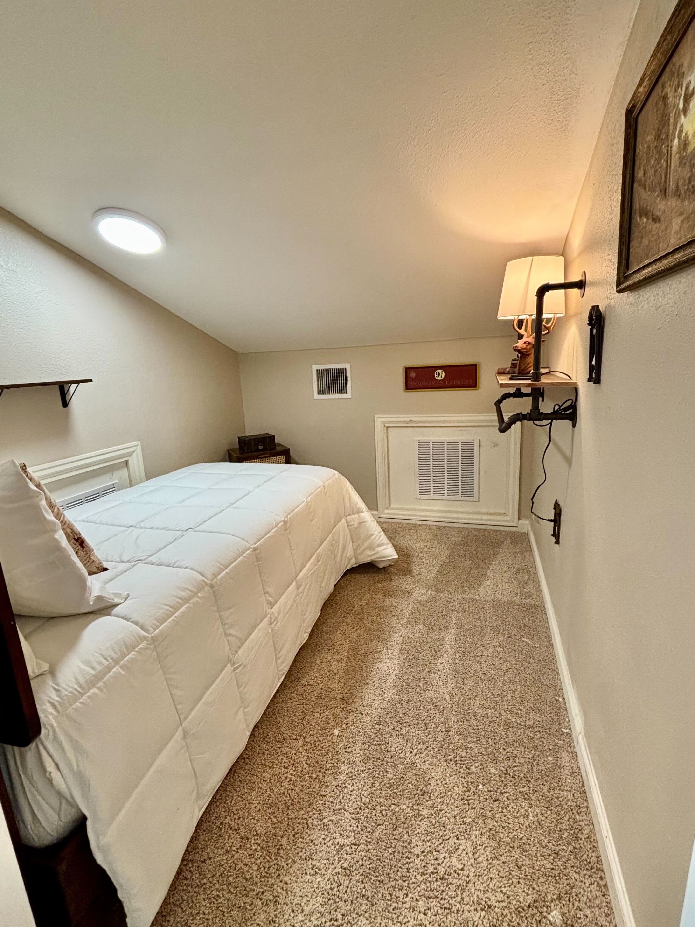 Ein Schlafzimmer mit einem Bett, einem Heizkörper, einer Wandlampe und einem kleinen Regal mit einem dekorativen Gegenstand.