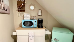 Een kitchenette met een magnetron, koffiezetapparaat en een kleine koelkast. Er zijn decoratieve wandpanelen en een prullenbak.