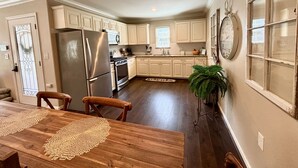 A kitchen with white cabinets, stainless steel appliances, and a wooden dining table with placemats. - The Vine (New Ulm)