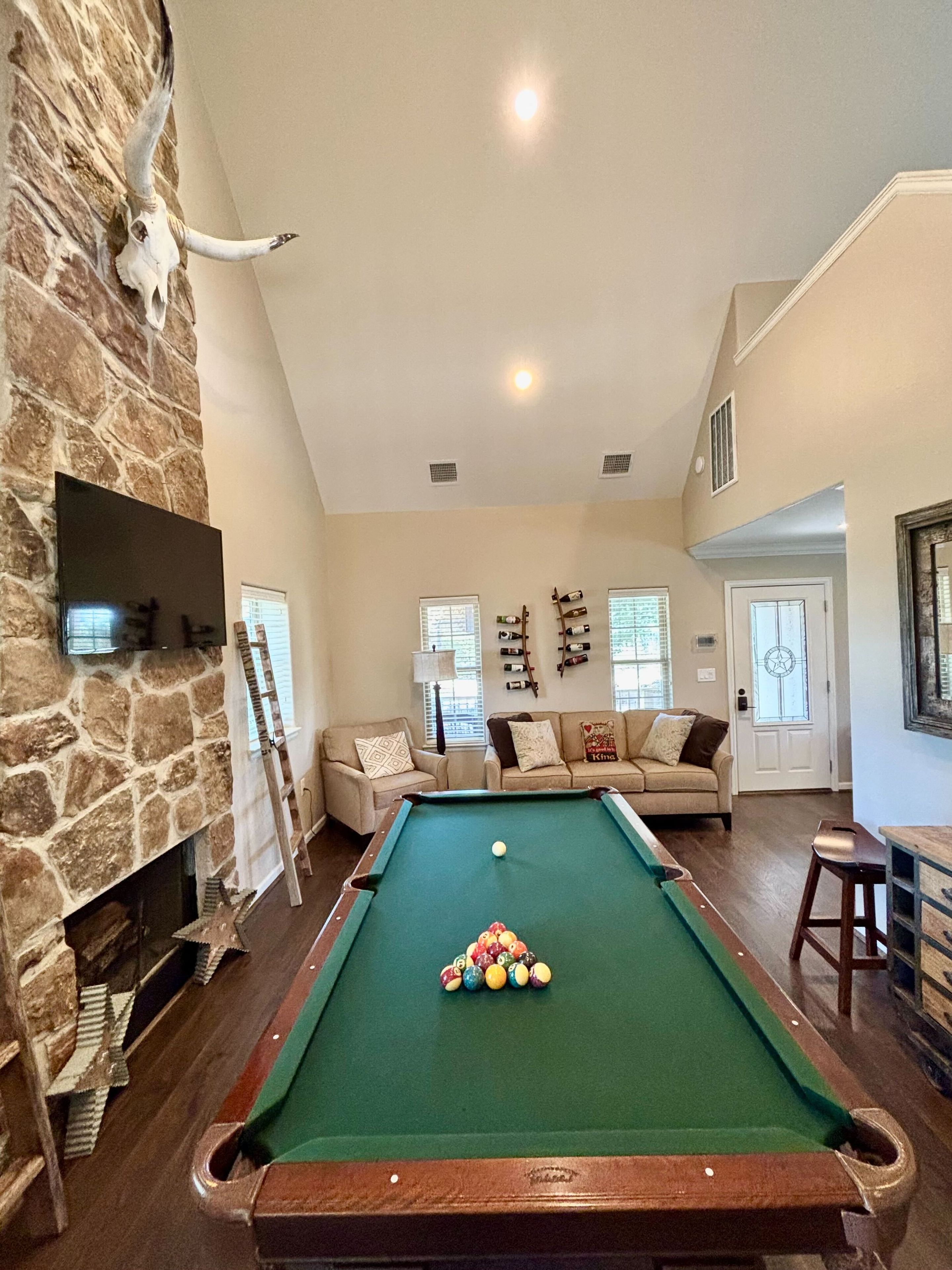 A pool table in a living room with a stone wall and a mounted TV.