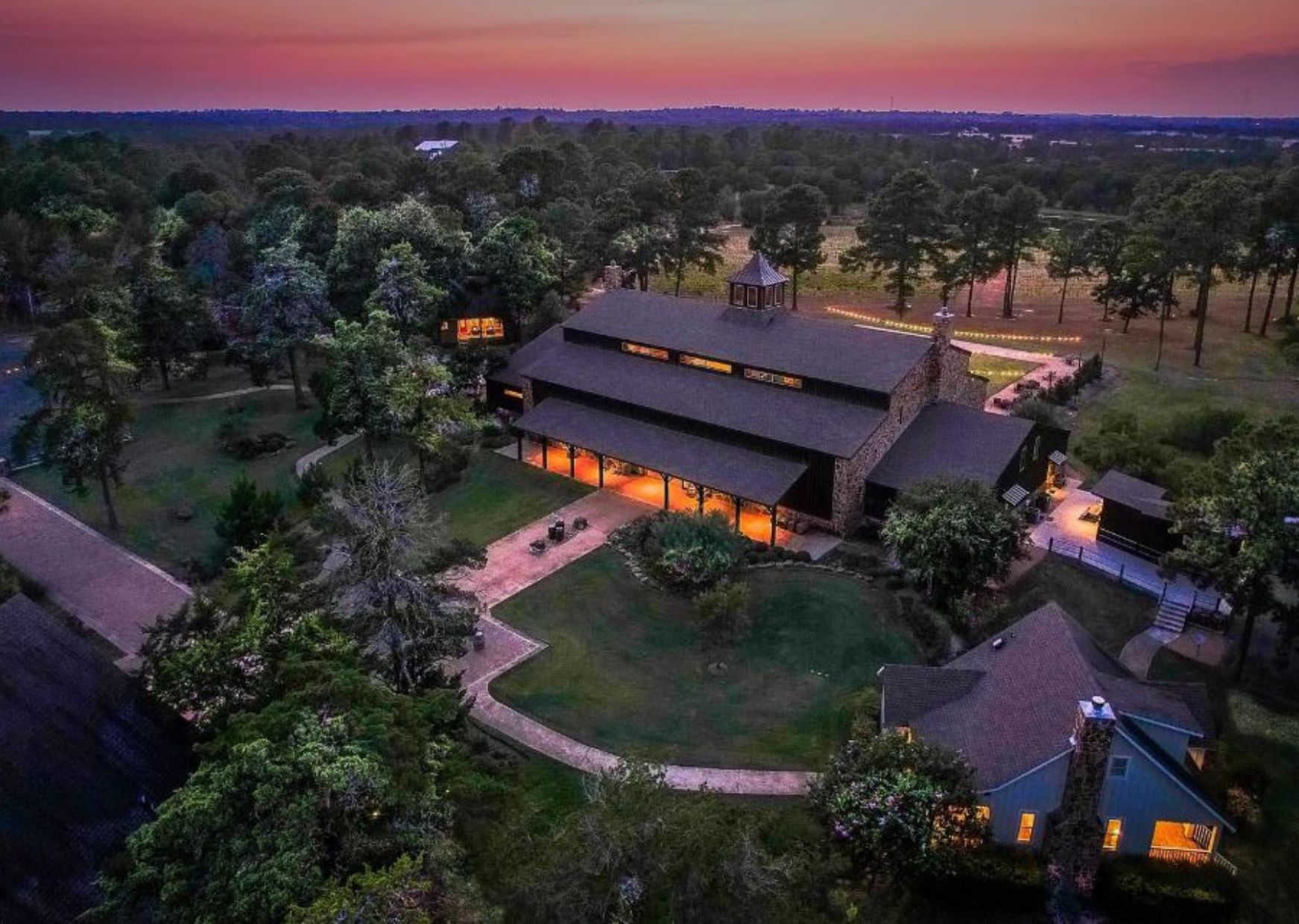 A large, modern building with multiple sections, surrounded by lush greenery and a well-maintained lawn.