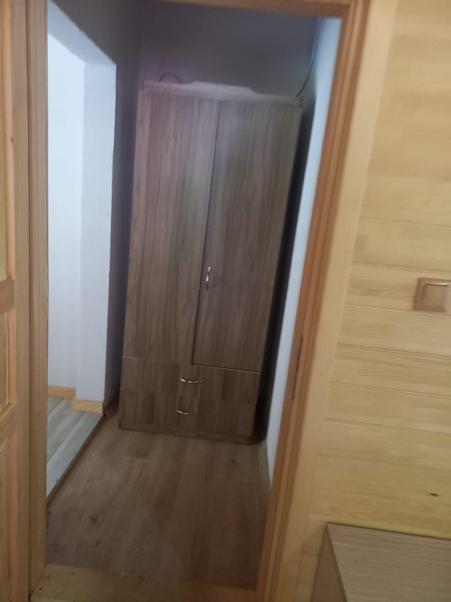 Ein schmaler Flur mit einem Holzschrank und einer Tür links.